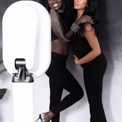 Photobooth Two women posing together in front of a white photo booth with a plant to the side against a dark gradient backdrop.